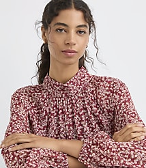 A woman with dark curly hair and a floral print blouse is posed against a plain white background. carousel Product Image 2
