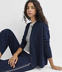 A woman in a navy cardigan and grey t-shirt sits on a white floor with navy pants, against a plain white background. carousel Product Image 1