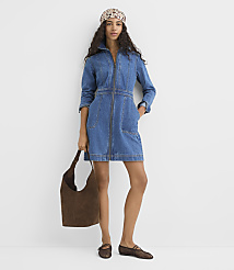 A woman in a denim dress and patterned headscarf stands against a plain white background, holding a brown suede bag and wearing brown flats. carousel Product Image 1