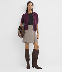 A woman in a burgundy cardigan, black top, and patterned skirt stands against a plain white background, wearing brown boots and carrying a brown bag. carousel Product Image 2
