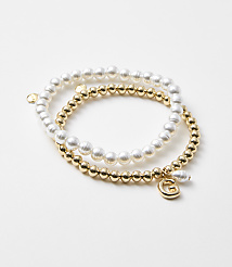 Two bracelets, one with white pearls and the other with gold beads and a "G" charm, rest on a plain white background. carousel Product Image 1