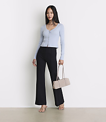 A woman in a light blue cardigan and black flared pants stands with a beige handbag against a plain white background. carousel Product Image 1
