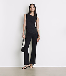 A woman in a black tank top and flared pants stands against a plain white background, holding a small black purse. carousel Product Image 1