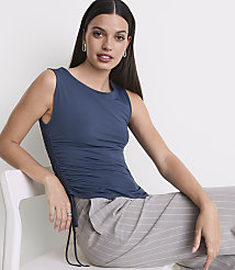 A woman in a blue ruched tank top and striped pants sits on a white chair against a plain white background. carousel Product Image 2