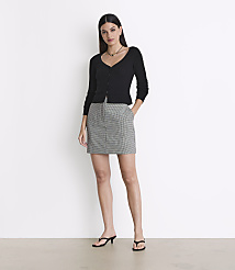 A woman in a black cardigan and a checkered skirt stands against a plain white background. carousel Product Image 1