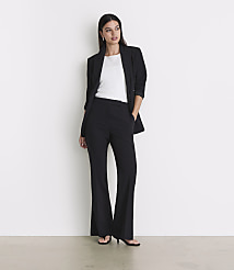 A woman in a black blazer and flared pants stands against a plain white background with a light gray floor in the foreground. carousel Product Image 1