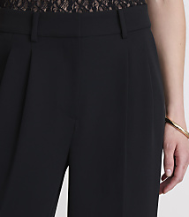 Black pleated trousers are in the foreground, with a person's arm and a gold bracelet visible on the right, and a hint of lace fabric at the top. carousel Product Image 4