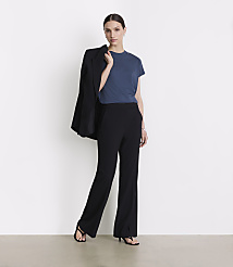 A woman in a blue t-shirt and black pants stands against a white background, with a black blazer draped over her shoulder. carousel Product Image 1