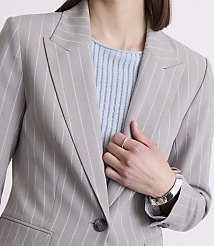 A woman in a pinstripe blazer and light blue top poses with her hand on her chest, against a plain background. carousel Product Image 5