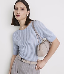 A woman in a light blue ribbed top and pinstripe pants poses with a small beige handbag against a plain white background. carousel Product Image 2