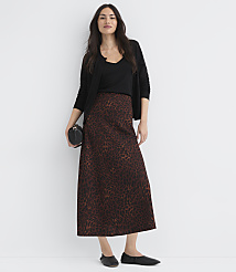 A woman in a leopard print skirt and black top stands against a plain white background, holding a small black purse. carousel Product Image 1