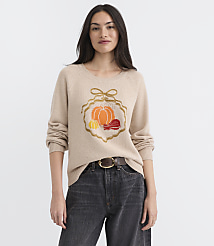A woman in a beige sweater with an embroidered pumpkin and macarons stands against a plain white background. carousel Product Image 2