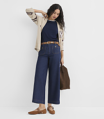 A woman in a navy shirt, beige cardigan, and wide-leg jeans stands against a plain white background, holding a brown bag. carousel Product Image 1