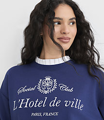 A woman in a blue sweatshirt with a white ruffled collar stands against a plain white background. carousel Product Image 5