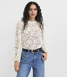 A woman in a cream lace top and blue jeans stands against a plain white background. carousel Product Image 1