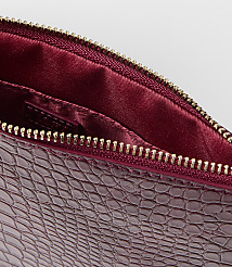 A close-up of a burgundy embossed leather clutch with a gold zipper is set against a plain white background. carousel Product Image 2