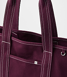 A close-up of a burgundy canvas tote bag with white stitching and a small logo is presented against a plain white background. carousel Product Image 2