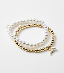 Two bracelets, one of pearls and one of gold beads with a charm, rest on a plain white background. carousel Product Image 1