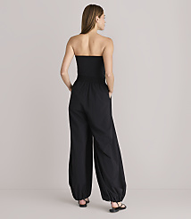 A woman in a black strapless jumpsuit stands with her hands in her pockets against a plain white background. carousel Product Image 3