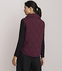 A woman in a quilted burgundy vest and black clothing stands against a plain, light-colored background. carousel Product Image 3
