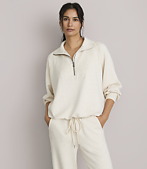 A woman in a cream-colored quarter-zip sweatshirt and matching pants stands against a plain, light gray background. carousel Product Image 1