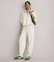 A woman in a cream loungewear set and green sneakers stands against a plain, light gray background. carousel Product Image 1