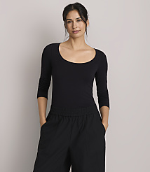 A woman in a black scoop-neck shirt and black pants stands against a plain gray background. carousel Product Image 1