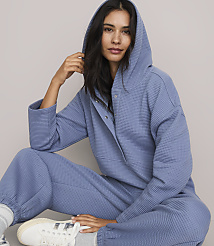 A woman in a blue waffle-knit loungewear set with a hood is seated against a plain, light gray background. carousel Product Image 2