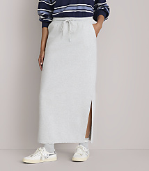 A person stands in a light gray maxi skirt with a side slit, paired with sneakers, against a plain, light-colored background. carousel Product Image 2