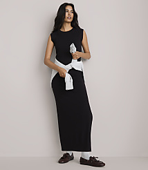 A woman in a black maxi dress and light blue sweater tied around her waist stands against a plain, light gray background. carousel Product Image 2
