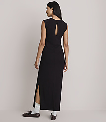 A woman in a black maxi dress with a cutout back and side slits stands with her back to the camera, wearing white socks and brown loafers against a plain, light-colored background. carousel Product Image 3