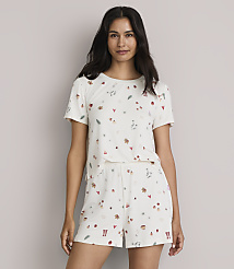 A woman in a cream-colored pajama set with a scattered pattern of small festive icons stands against a plain, light-colored background. carousel Product Image 1