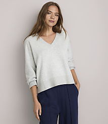 A woman in a light gray v-neck sweater and navy blue pants stands against a plain white background. carousel Product Image 1