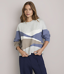 A woman in a patterned sweater and navy pants stands against a plain gray background. carousel Product Image 2
