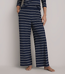 A person stands in wide-leg navy and white striped pajama pants with their hands in their pockets against a plain white background. carousel Product Image 2