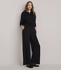 A woman in a black outfit stands with her hands in her pockets against a plain white background. carousel Product Image 1
