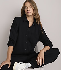A woman in a black jumpsuit sits in front of a plain white background. carousel Product Image 1