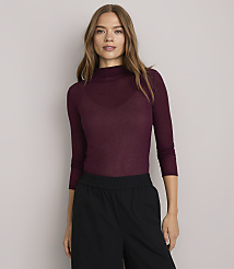A woman in a burgundy turtleneck and black pants stands against a plain white background. carousel Product Image 2
