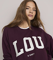 A young woman in a maroon sweatshirt with "LOU & GREY" printed on it is shown against a plain, light-colored background. carousel Product Image 4