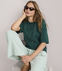 A young woman in a green v-neck sweater and light green pants stands against a plain gray background. carousel Product Image 2