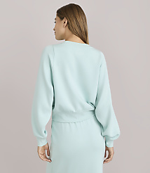 A woman in a light blue sweatshirt and skirt stands against a plain, light gray background. carousel Product Image 4