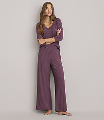 A woman in striped pajamas stands with her arms crossed against a plain gray background.
