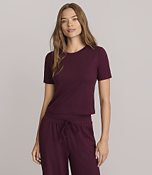 A woman in a maroon t-shirt and matching pants stands against a plain gray background.