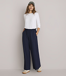 A woman in a white shirt, navy pants, and a green cap stands with her hands in her pockets against a plain white background. carousel Product Image 1