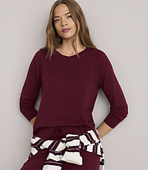 A woman in a maroon sweater and pants stands against a plain gray background, with a striped sweater tied around her waist. carousel Product Image 1