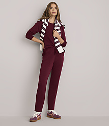 A woman in a burgundy loungewear set and striped sweater stands against a plain white background.