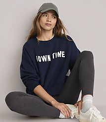 A woman in a navy sweatshirt and grey leggings sits on a white floor, with a plain grey background. carousel Product Image 2
