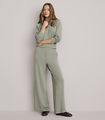 A young woman in a sage green loungewear set stands against a plain white background.