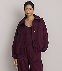 A woman in a maroon tracksuit stands against a plain, light gray background. carousel Product Image 1