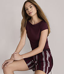 A young woman with long brown hair, wearing a maroon t-shirt and striped shorts, sits against a plain white background. carousel Product Image 2